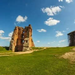 Ruiny opuszczonego zamku w Polsce, z wieżą w rusztowaniach, na tle błękitnego nieba z chmurami.