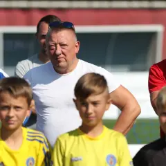 Marek Śledź, trener, w białej koszulce, stoi wśród młodych piłkarzy na boisku.