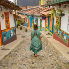 Una mujer camina por una calle empedrada entre casas coloridas, un ejemplo vibrante de los pueblos de Colombia.