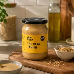 Słoik z napisem "The Real Tahini" obok miseczki z ziarnami sezamu i cytryną. Tahini to pasta z sezamu, idealna do hummusu.