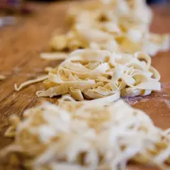 Frische Pasta, bereit für ein köstliches Pasta fresca Rezept, liegt auf einem Holztisch.
