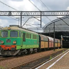 Zielona lokomotywa ST43-238 z wagonami towarowymi na torach kolejowych, pod zadaszeniem dworca.