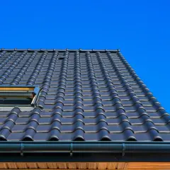 Toit en tuiles sombres, avec deux fenêtres de toit ouvertes, sous un ciel bleu vif. Ces matériaux de couverture sont bien posés.