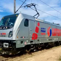 Srebrna lokomotywa Traxx z napisem LOTOS i hasłem "we connect Poland together" stoi na torach.