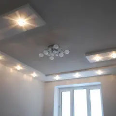 Nowoczesny sufit z wieloma punktami świetlnymi, tworzącymi rozproszone światło. Centralnie umieszczony designerski żyrandol.