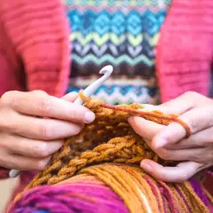 Mani che lavorano a maglia con un uncinetto, filato colorato e un maglione rosa. Nonostante sembri rilassante, lavorare a maglia fa male al cuore se si pensa troppo.