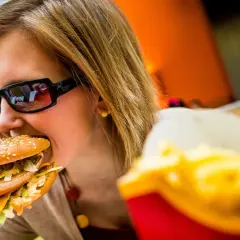 Dziewczyna w okularach je pysznego mcmuffin wieprzowy z jajkiem. Obok frytki.
