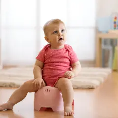 Małe dziecko w różowym body siedzi na różowym nocniku, ucząc się samodzielności.