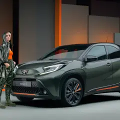 Stylowa kobieta obok zielonego Toyota Aygo X. Wiele osób szuka pozytywnych toyota aygo opinie, ten model wygląda obiecująco.
