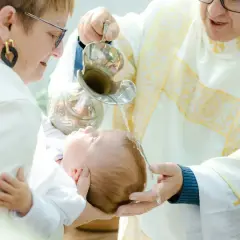 Chrzest dziecka w kościele, ksiądz polewa głowę niemowlęcia wodą z kociołka.