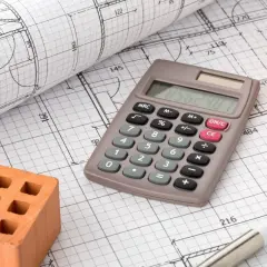 Calcolatrice, mattoni e rotolo di disegni tecnici: elementi essenziali per la pianificazione dell'urbanizzazione primaria.