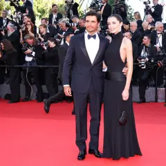 A couple in formal wear on a red carpet, surrounded by photographers.