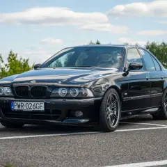 Czarne BMW E39 na parkingu, z widocznym przodem i bokiem samochodu.