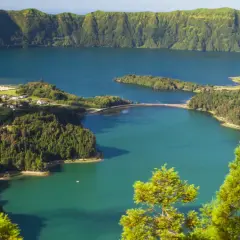 Malowniczy krajobraz portugalskiego archipelagu na Atlantyku: jezioro w kraterze wulkanicznym, otoczone zielonymi wzgórzami i niewielką wioską.