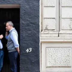 50mm street photography captures two men in conversation by a doorway numbered 43, while another man looks at his phone.