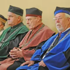 Czterech mężczyzn w togach akademickich i czapkach rektora siedzi w rzędzie.