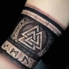 Tatuaże wikingów na przedramieniu: symbol Walhalla i runy, wyglądające jak wyryte na kamieniu.