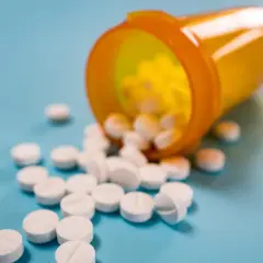 Białe tabletki rozsypane z pomarańczowego pojemnika. Mogą to być leki immunosupresyjne, które pomagają w transplantacjach.