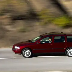 Czerwone volvo v70 ii jedzie po drodze, za kierownicą siedzi kobieta. Rozmyte tło sugeruje ruch.