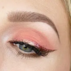 En närbild på ett öga med en vacker rosa sminkning. Ögonlocket har en mjuk rosa skugga och en glittrig eyeliner i guld och rosa.