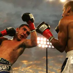 Two boxers clash in a dramatic boxing round, sweat flying as they exchange blows under stadium lights.