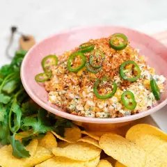En krämig mexikansk majssallad toppad med jalapeños och serverad med tortillachips och färsk koriander.