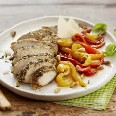 Sabroso pollo con pimientos asados, piñones y queso parmesano, servido en un plato blanco sobre una mesa de madera.