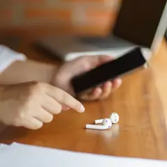 Osoba trzyma telefon, obok leżą białe słuchawki. Może to być powód, dla którego dźwięk przez Bluetooth przerywa na Androidzie.