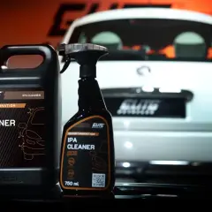 Dwa opakowania IPA CLEANER, alkohol izopropylowy do detailingu, obok białego samochodu.