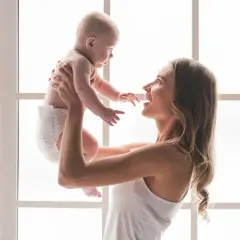 Szczęśliwa mama podrzuca w górę swoje 7 miesięczne dziecko.