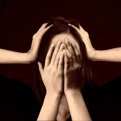Dłonie zakrywają twarz, włosy opadają, a ramiona zaciskają się na głowie. To obraz głębokich emocji samoświadomościowych, wewnętrznego zmagania.
