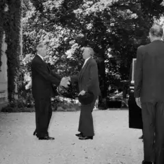 Konrad Adenauer und Charles de Gaulle schütteln sich die Hände. Ein Mann im Anzug steht daneben.