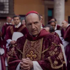 Scena z filmu o papieżu. Kardynał w bogato zdobionej szacie z czerwonym piuską. W tle inni duchowni.