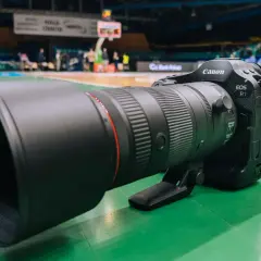 Profesjonalny obiektyw Canon EOS R1 z teleobiektywem 70-200mm na zielonej podłodze hali sportowej.