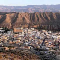 Pueblo blanco anidado en el **desierto de Tabernas**, con colinas áridas y montañas al fondo.