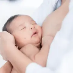 Niemowlę pręży się i wygina podczas karmienia, wtulone w ramiona mamy.