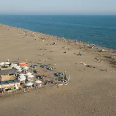 Vue aérienne d'une plage privée au Grau-du-Roi, avec des parasols, des transats et des baigneurs profitant du soleil et de la mer.