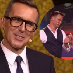 Uśmiechnięty mężczyzna w okularach i garniturze, w tle okrągłe zdjęcie pary, która trzyma się za ręce. To czar par Cichopek.