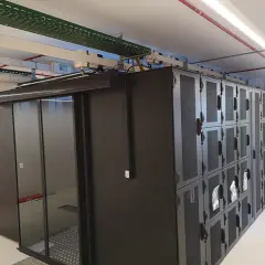 Un micro data center avec des baies de serveurs noires et une porte vitrée. Des câbles et des conduits sont visibles au plafond.