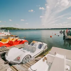 Kolorowe rowerki wodne i żaglówki czekają na gości nad spokojnym jeziorem w Czaplinku.