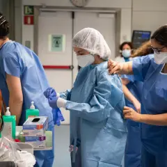 Pielęgniarki w strojach ochronnych przygotowują się do pracy. W tle sprzęt medyczny i inne osoby w fartuchach. To pokazuje, co może odliczyć pielęgniarka na kontrakcie.