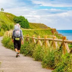 Vandrare på el camino de Santiago längs en kuststig med havet till höger och en grön kulle till vänster.