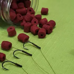 Czerwone kulki zanętowe i trzy haczyki wędkarskie gotowe do akcji.