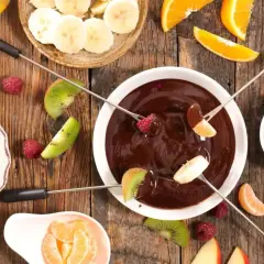 Pyszne fondue czekoladowe z malinami, bananami, kiwi i mandarynkami na drewnianym stole. Idealne na deser!