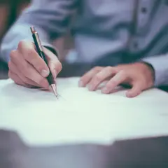 Mężczyzna pisze ręcznie dokument, który może być wzorem skargi na zarządcę nieruchomości.