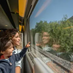 Bambino e madre guardano fuori dal finestrino del treno, indicando qualcosa. Un'ottima idea per i giochi da fare in treno, osservando il paesaggio che scorre.