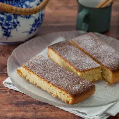 Saftiger mandelkuchen vom blech, bestäubt mit Puderzucker, auf einem Glas-Teller.
