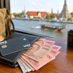 Geld wechseln in Bangkok: Thai Baht, DKB Visa Debitkarte, Hut, Tasche und Kamera liegen bereit für die Reise.