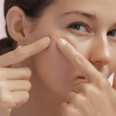 Une jeune femme examine un bouton sur sa joue, un signe possible pour savoir si on a une peau grasse.