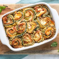 Involtini di zucchine al forno, dorati e filanti, con prosciutto e formaggio, guarniti con basilico fresco.